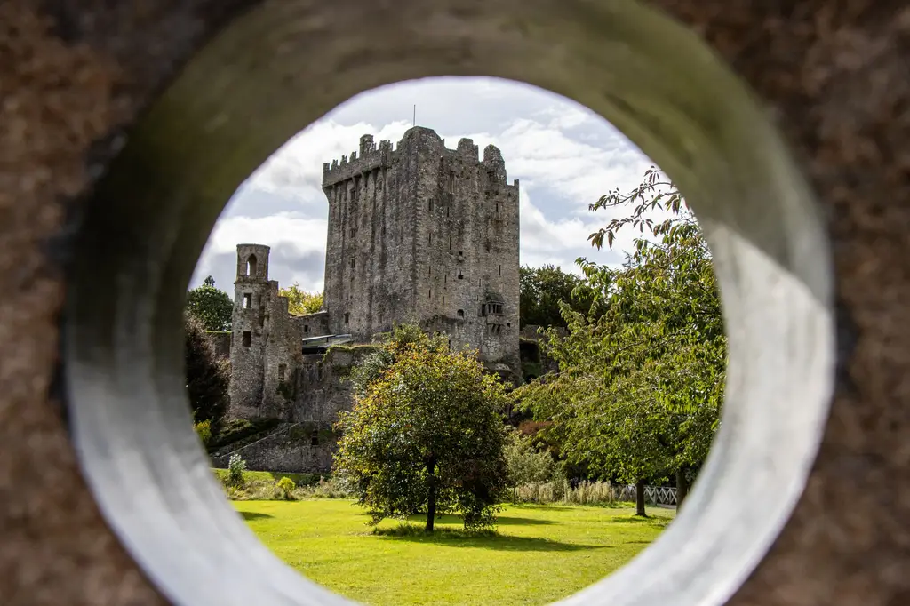 View of Blarney Castle in County Cork, Ireland, framed by a stone arch, under sunny skies.
