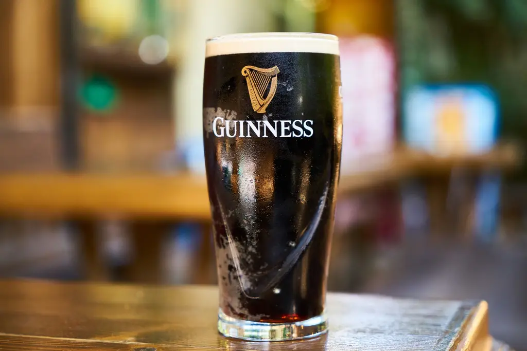 Close-up of a pint of Guinness stout beer on a wooden table in an indoor setting.