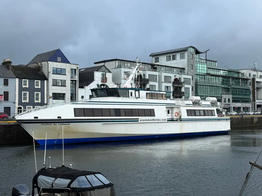 Aran Island ferry moored at Galway harbor with cityscape backdrop.