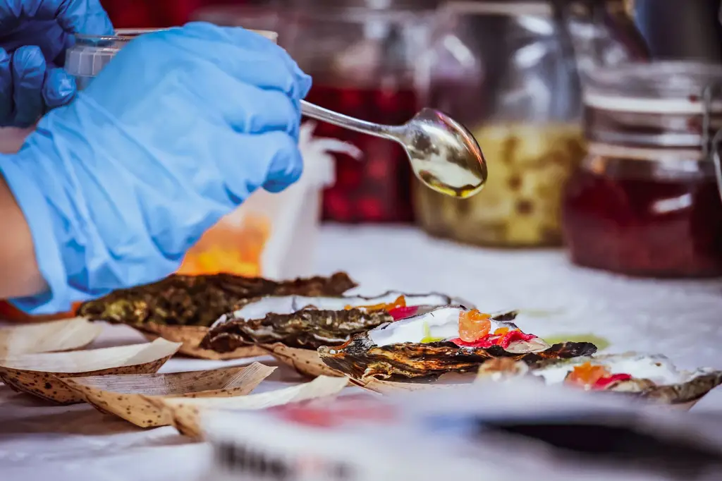 Chef preparing delicious oysters with sauce at a market stall.