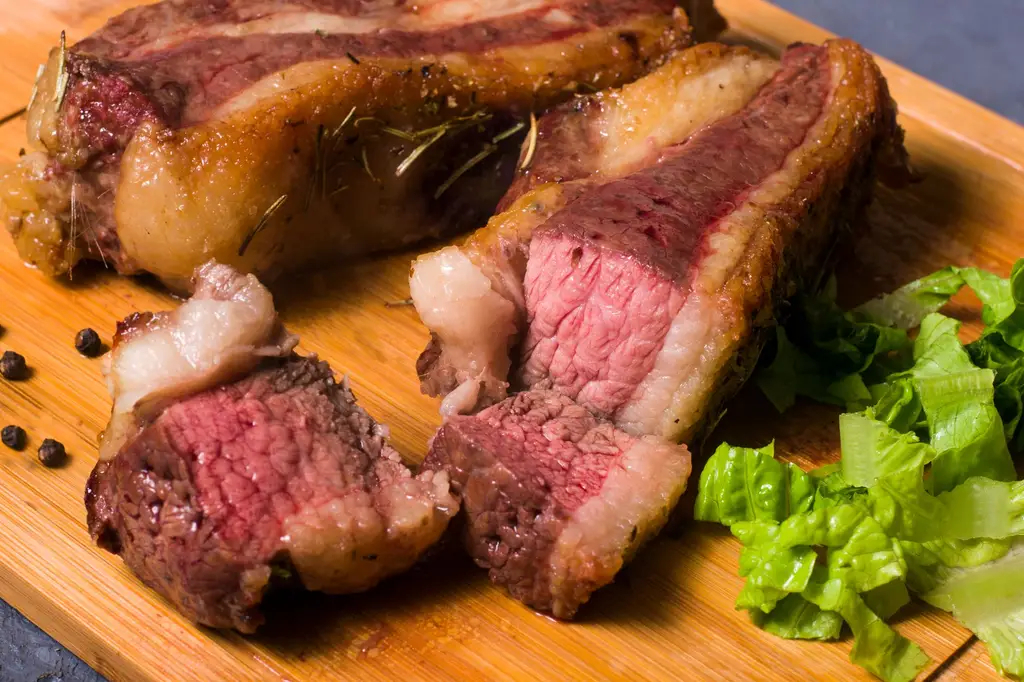 Close-up of sliced grilled steak with lettuce and peppercorns on a wooden board.