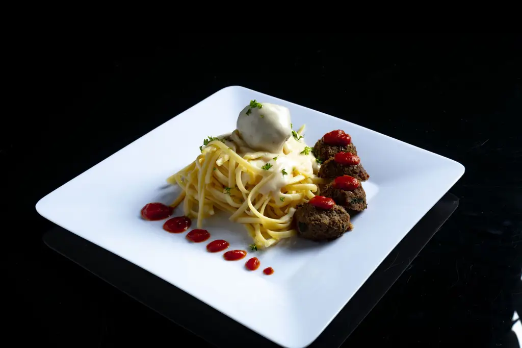 A gourmet dish featuring spaghetti with creamy sauce and meatballs served on a white plate.