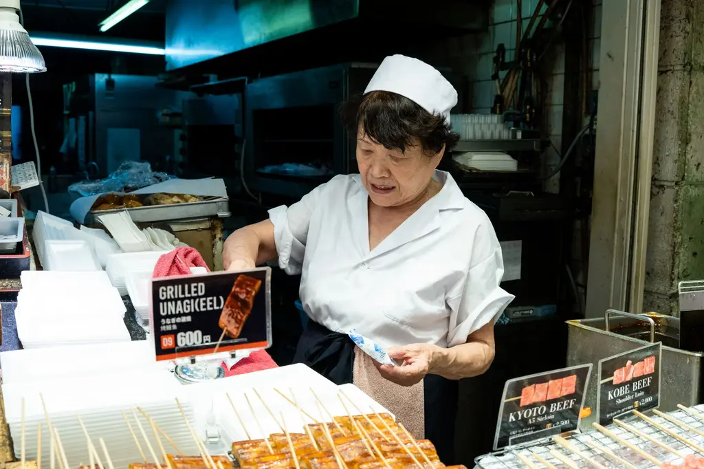 Japanese chef preparing grilled unagi skewers in a market setting, showcasing traditional street food.