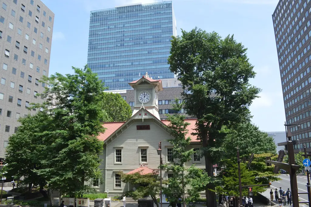 Daytime view of Sapporo's iconic clock tower surrounded by modern buildings and trees.