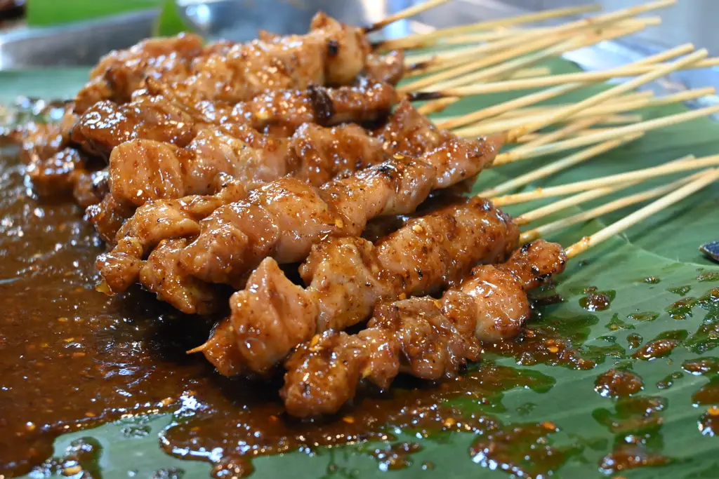 DFC 2193 Sticky char-grilled skewers of savory satay glazed in a rich peanut sauce resting on a banana leaf