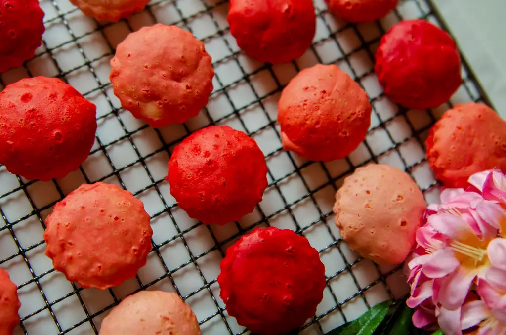 Top view of vibrant pink and red kuih apam on a cooling rack with floral decor from Malaysia.