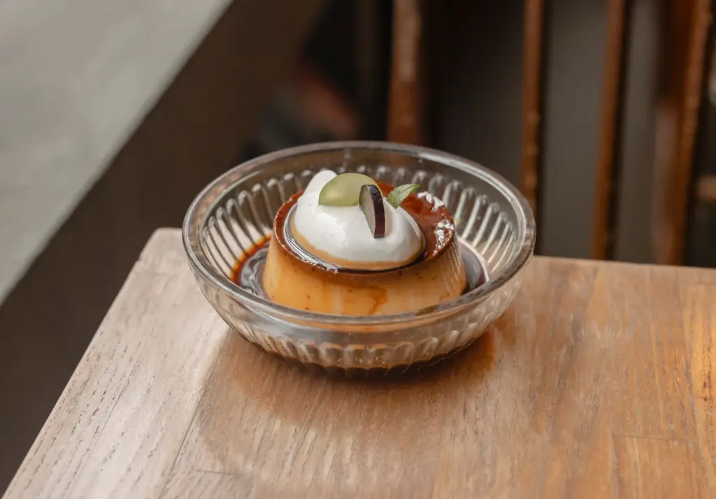 Close-up of a delicious custard dessert topped with cream and fruit, served in a glass bowl.
