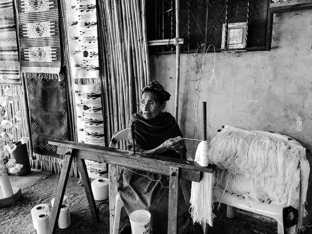 An elder artisan weaving carpets in a traditional workshop, Teotitlan del Valle, Mexico.