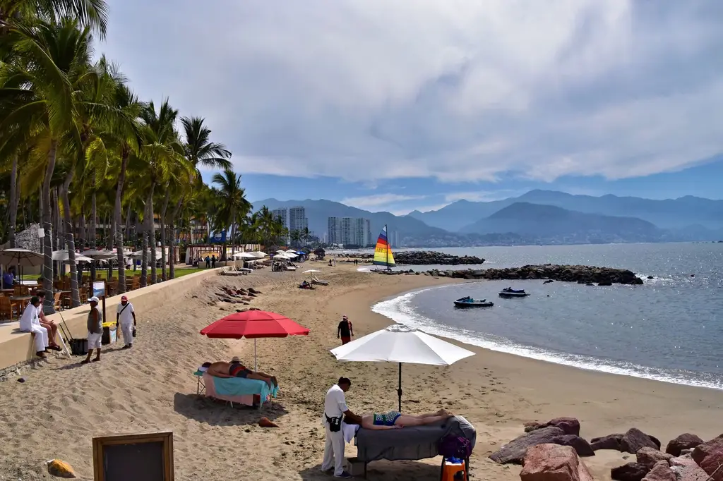 A serene beach view in Puerto Vallarta with palm trees, umbrellas, and a sailboat.