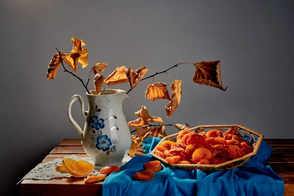 A beautifully composed autumn still life featuring dried apricots and a decorative jug with fall foliage.