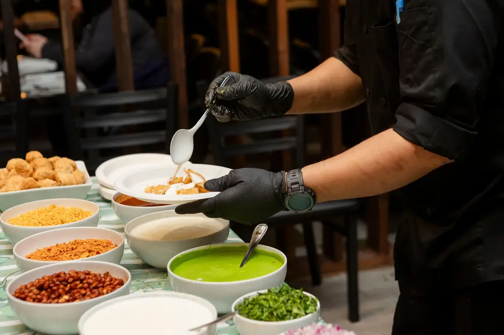 Chef skillfully preparing traditional Indian street food chaat with various toppings and sauces.