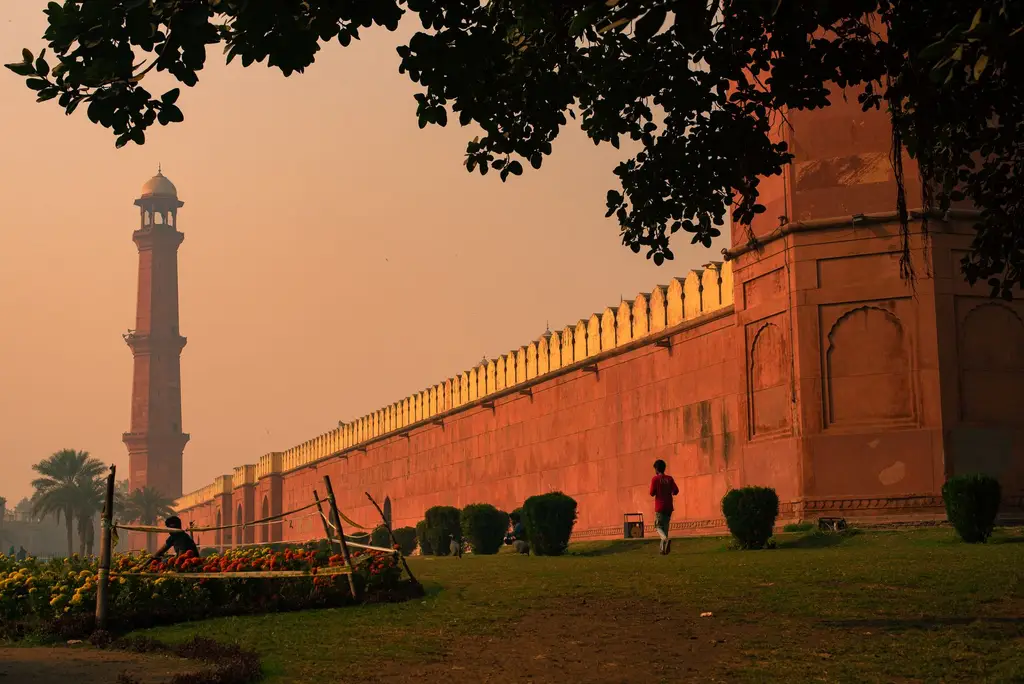 Silhouette of Badshahi Mosque minaret at sunset with trees in the foreground in Lahore, Pakistan.