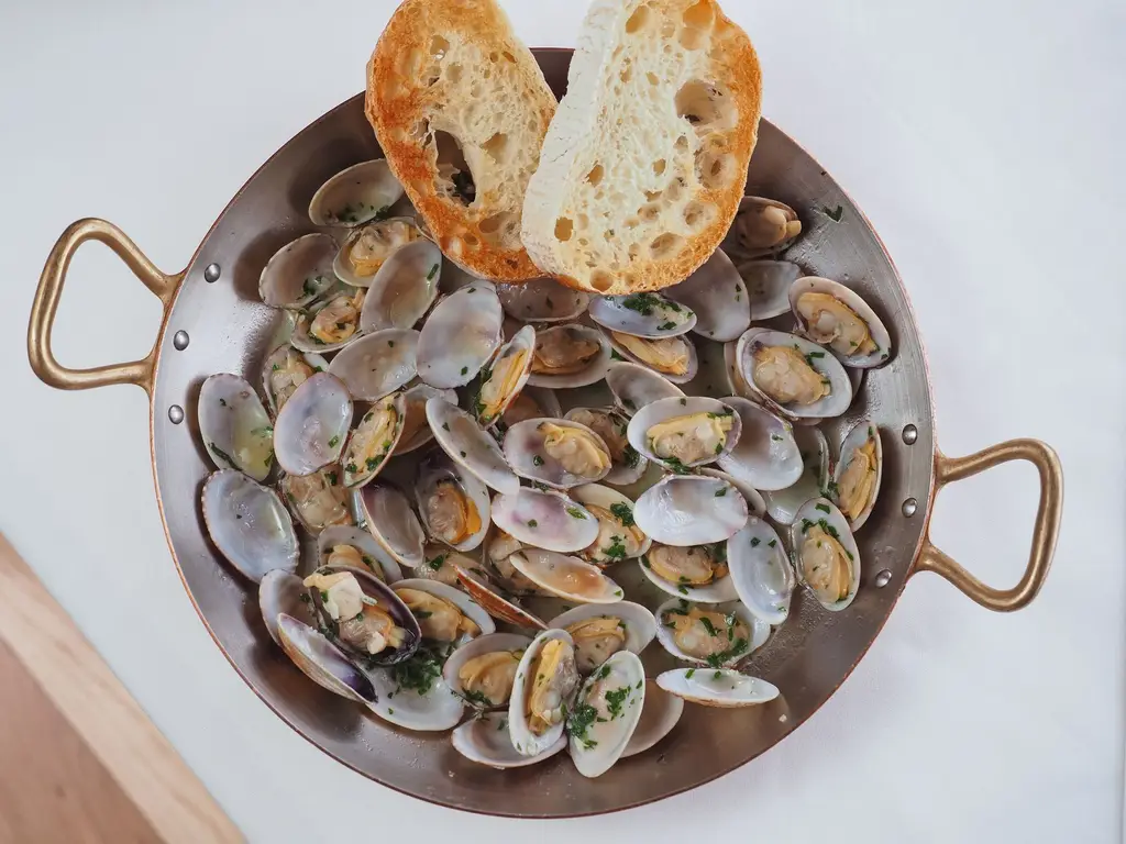 A delicious seafood dish featuring clams with garlic bread served in a copper saucepan, shot from above.