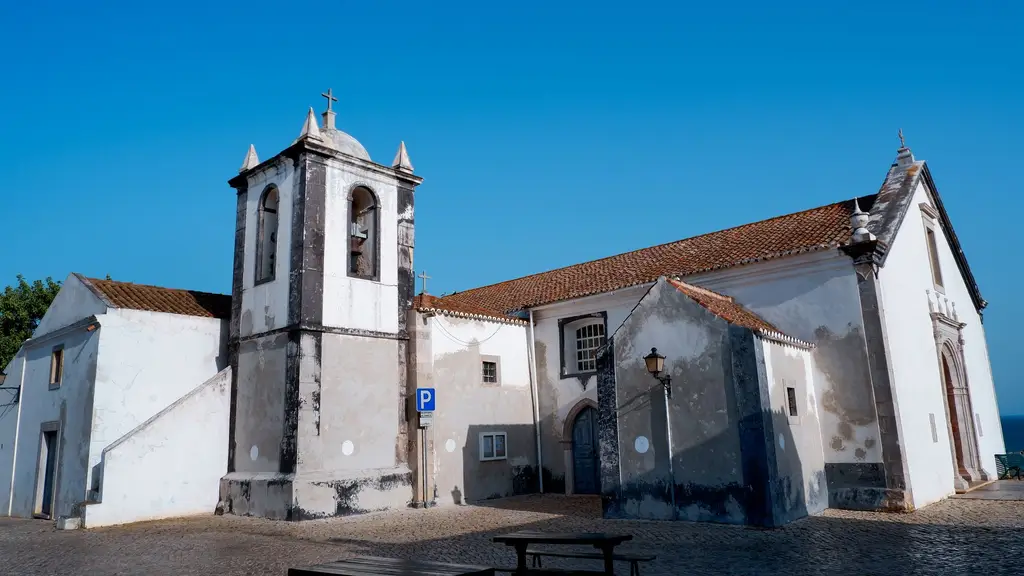 Sunlit church with a bell tower in Cacela Velha, Portugal under a clear blue sky.