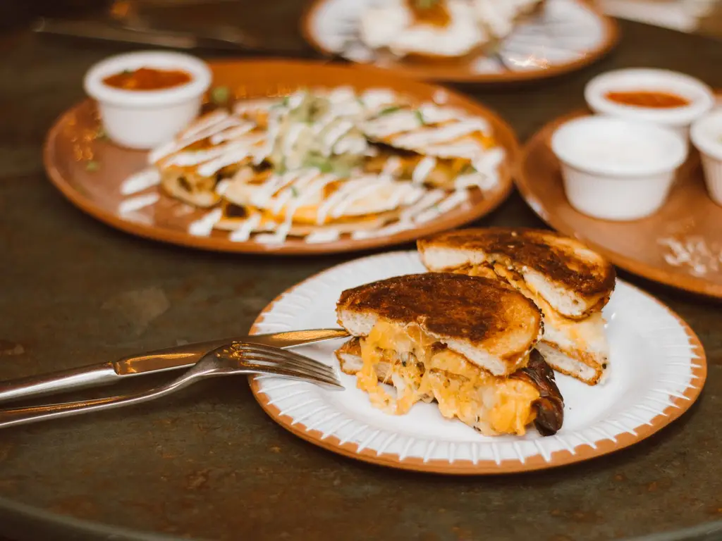 Mouthwatering grilled cheese sandwich with sides of sauces on a ceramic plate.