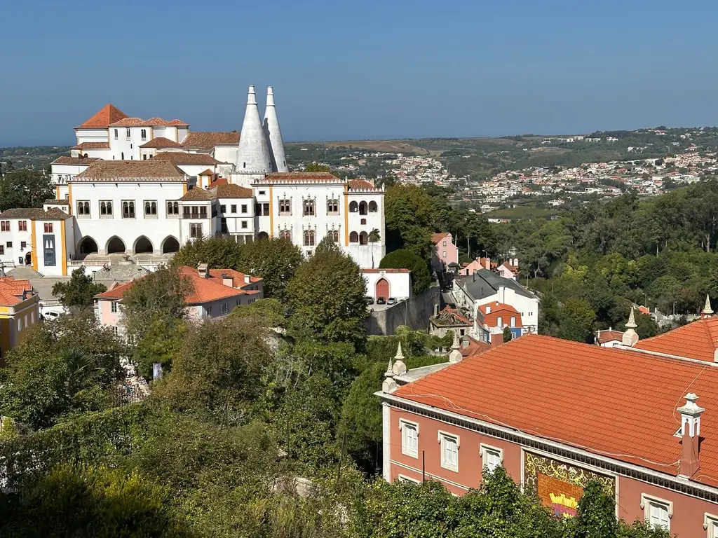 A scenic view of the Sintra National Palace surrounded by rooftops and lush greenery in Portugal.