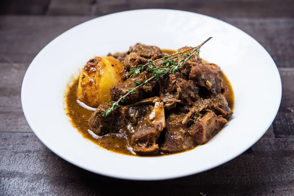 Close-up of savory Caribbean oxtail stew with potatoes served on a white plate.