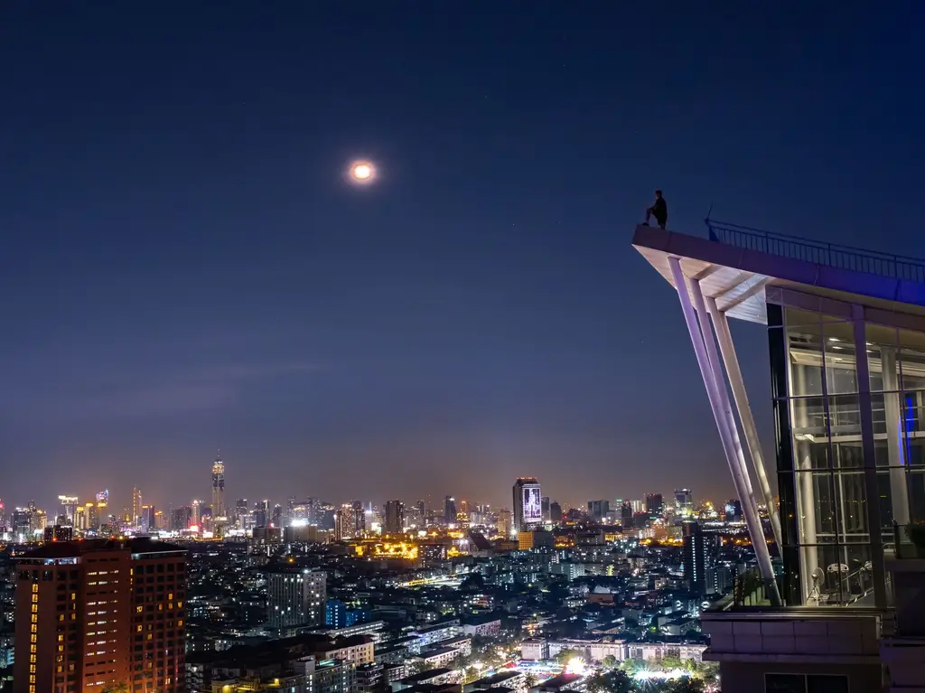 Stunning view of Bangkok's skyline under a full moon, capturing urban lights and architecture.