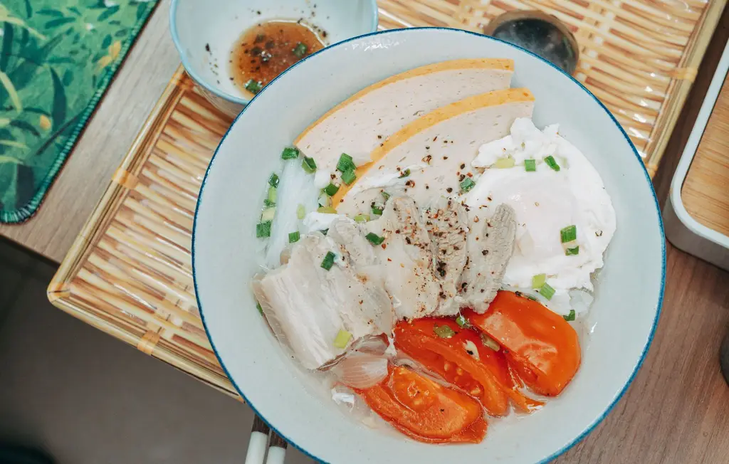 Delicious Vietnamese Pho with sliced pork, egg, tomatoes, and garnish on a bamboo mat setting.