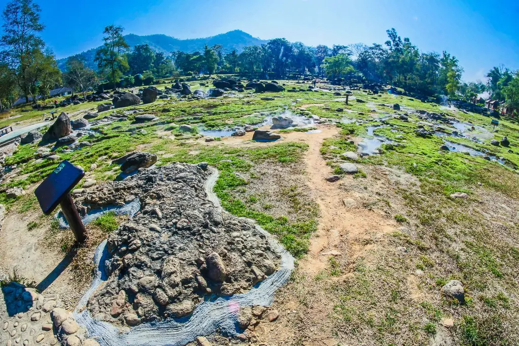 Vibrant landscape featuring natural hot springs with rocks and green patches under a clear sky.