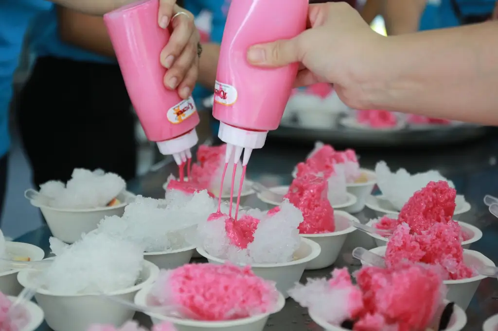Hands adding syrup to shaved ice desserts creating vibrant treats.