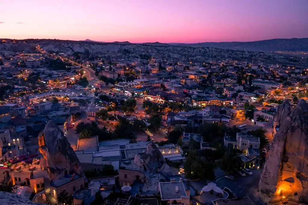 Stunning aerial view of Göreme, Turkey at twilight showcasing unique rock formations and vibrant city lights.