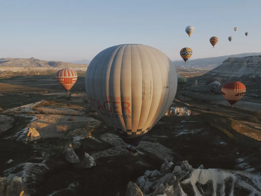 Scenic aerial view of colorful hot air balloons floating over Cappadocia's unique rock formations at sunrise.