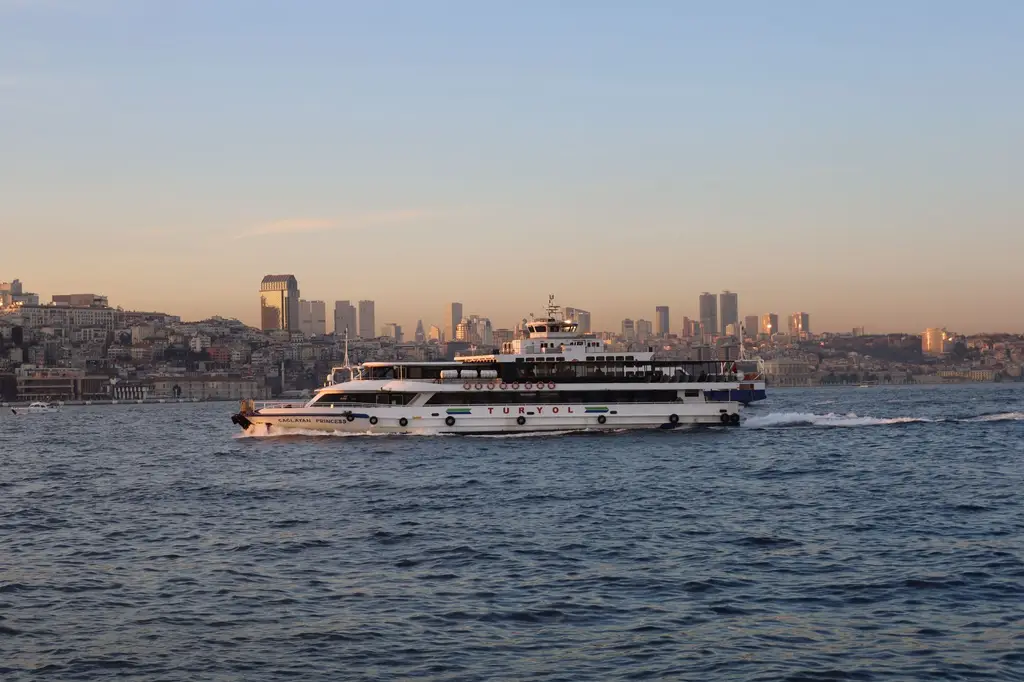 A ferry sails across the Bosphorus with Istanbul's skyline in the background during sunset.