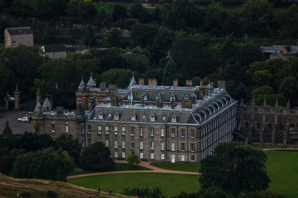 Stunning aerial shot of the historic Palace of Holyroodhouse surrounded by lush greenery in Edinburgh, Scotland.