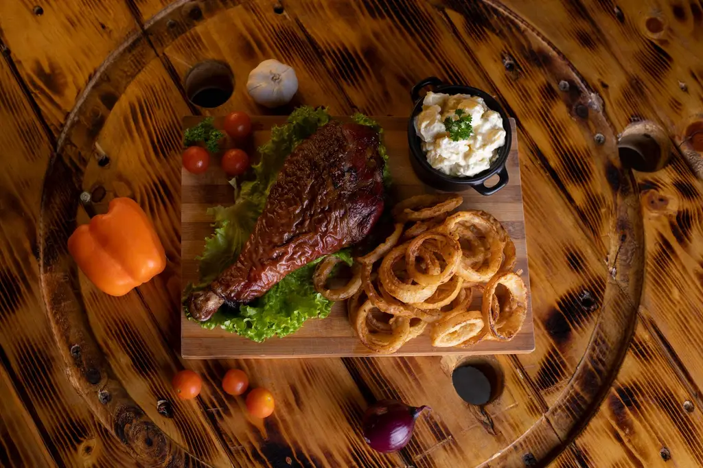 Delicious turkey leg served with onion rings and potato salad on a wooden table.
