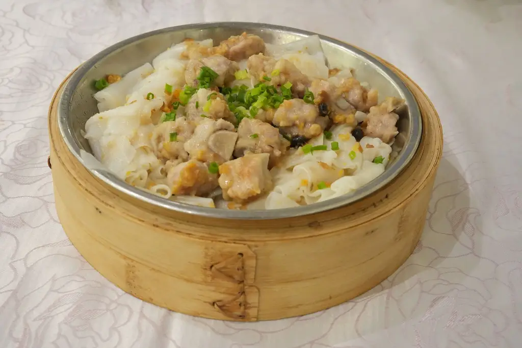 Steamed dim sum dish featuring pork and rice noodles in a bamboo steamer, garnished with chives.