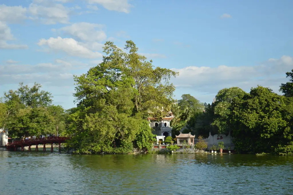 Serene view of Ngoc Son Temple and red bridge on Hoan Kiem Lake, Hanoi, under a clear blue sky.